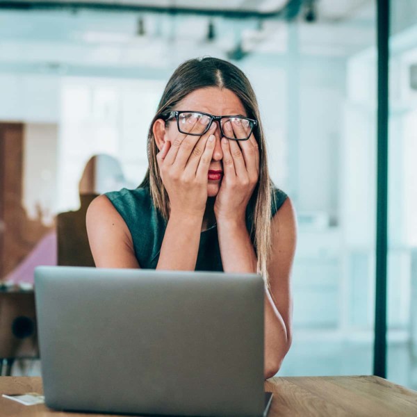 Image of someone rubbing their eyes while using their laptop.