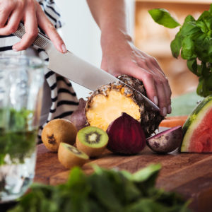 Person slicing a pineapple to put into their green juice