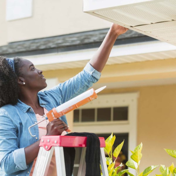 Woman fixing the siding of her house with caulk
