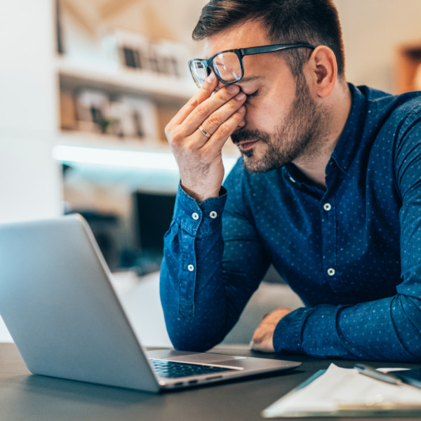 Image of someone rubbing their eyes while using a laptop.