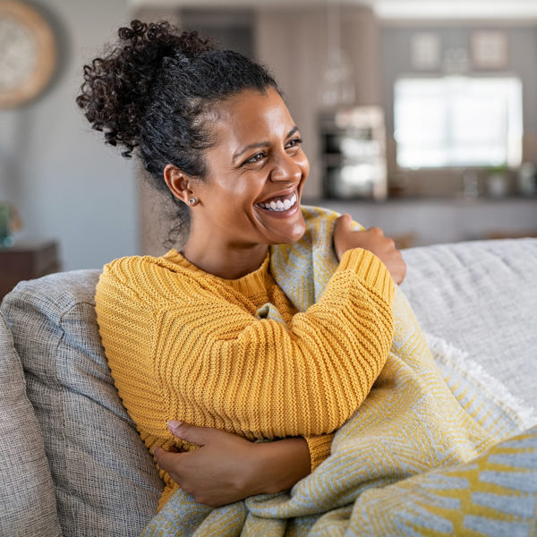 image of a woman smiling on a couch covered in a blanket